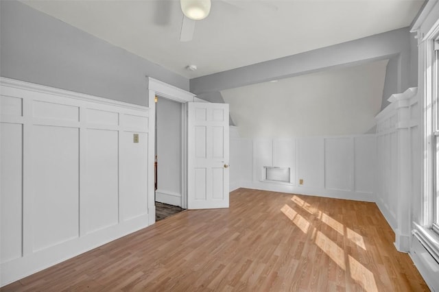 interior space featuring light wood-type flooring, a ceiling fan, and a decorative wall