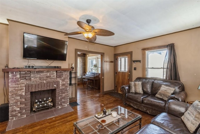 living area with dark wood-type flooring, ornamental molding, a brick fireplace, ceiling fan, and baseboards