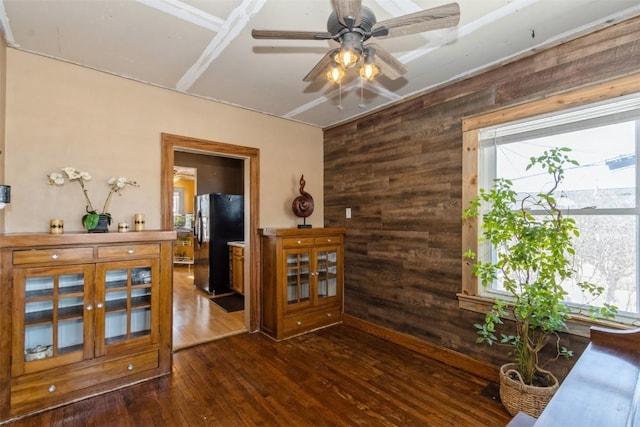 interior space with ceiling fan, dark wood-style flooring, and wooden walls