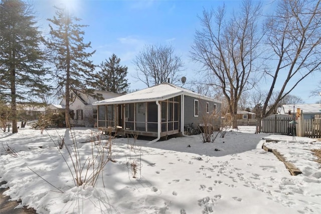 snow covered house with a sunroom and fence