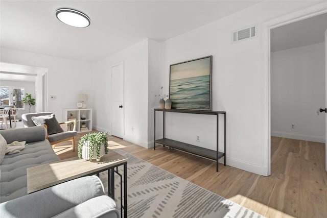 living room with light wood-type flooring, visible vents, and baseboards