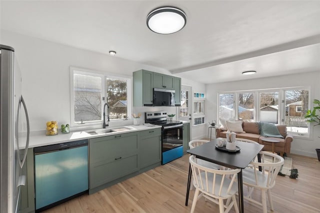 kitchen featuring light wood-style flooring, stainless steel appliances, light countertops, green cabinets, and a sink