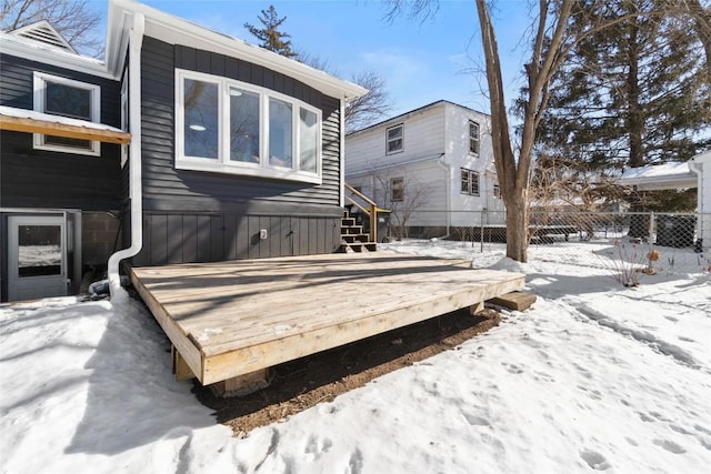 snow covered back of property featuring a deck and fence