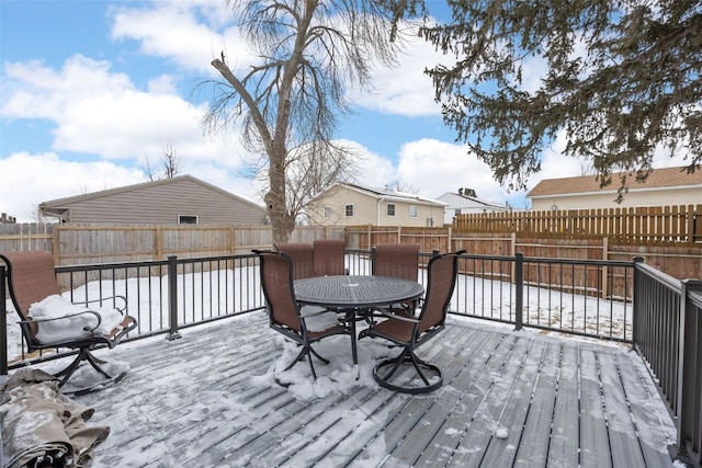 snow covered deck featuring outdoor dining area and a fenced backyard