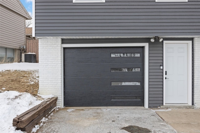 snow covered garage with cooling unit and concrete driveway