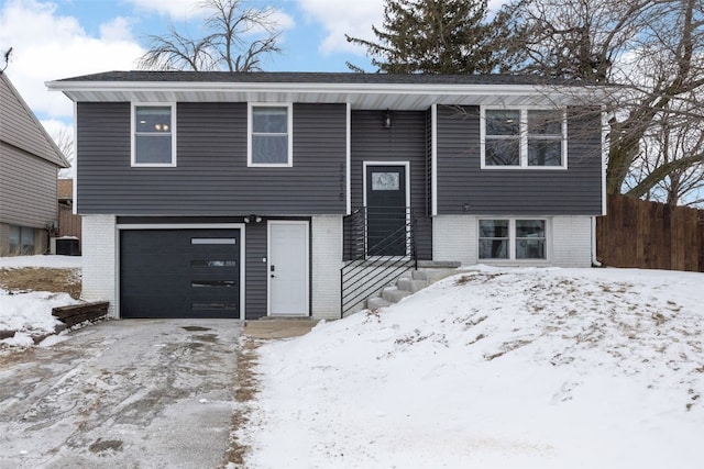 split foyer home with a garage, brick siding, fence, and central AC