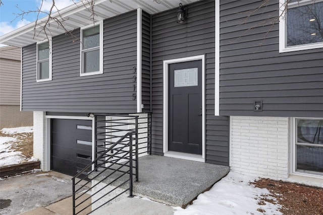 snow covered property entrance featuring a garage and brick siding