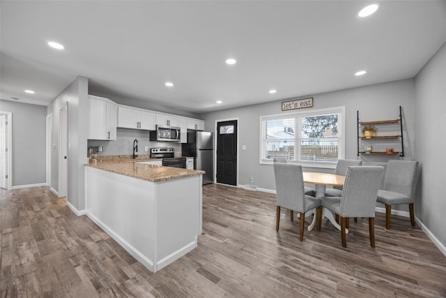 kitchen featuring recessed lighting, stainless steel appliances, a peninsula, white cabinetry, and light stone countertops