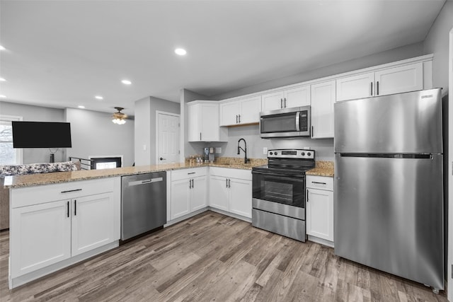 kitchen with stainless steel appliances, light wood-type flooring, white cabinetry, and light stone countertops