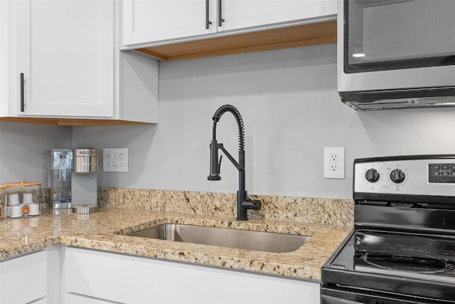 kitchen with white cabinets, light stone counters, stainless steel appliances, and a sink