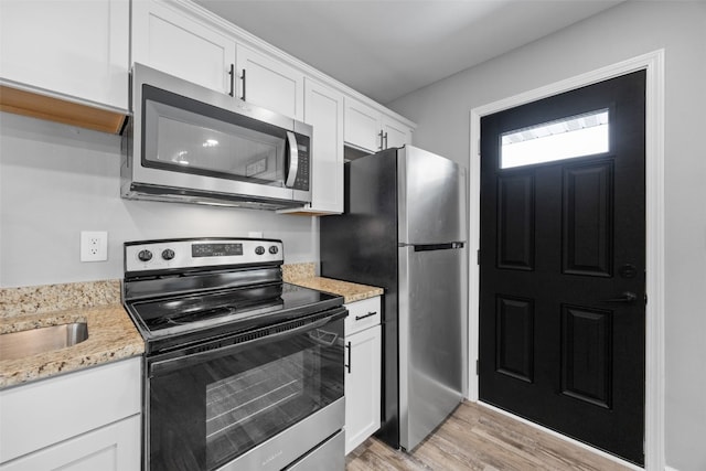 kitchen featuring light wood-type flooring, light stone countertops, white cabinetry, and stainless steel appliances