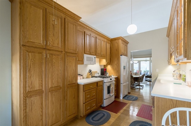 kitchen with white appliances, light wood finished floors, hanging light fixtures, light countertops, and a sink