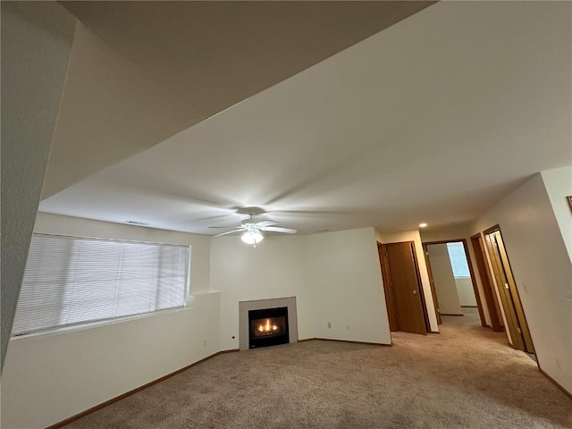 unfurnished living room featuring light carpet, a fireplace, baseboards, and ceiling fan