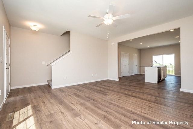 unfurnished living room featuring baseboards, ceiling fan, stairway, wood finished floors, and a sink