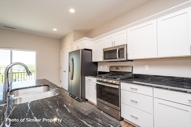 kitchen featuring appliances with stainless steel finishes, dark stone counters, white cabinets, and a sink