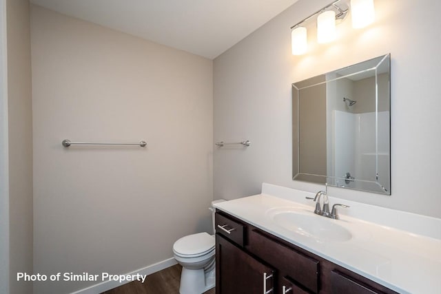 bathroom featuring a shower, toilet, vanity, wood finished floors, and baseboards