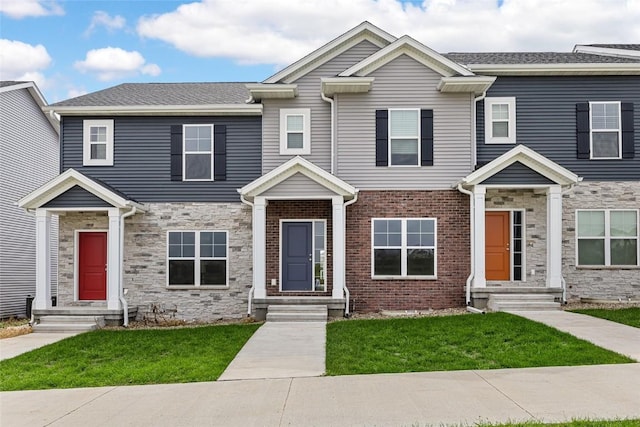 view of property featuring entry steps, stone siding, brick siding, and a front yard