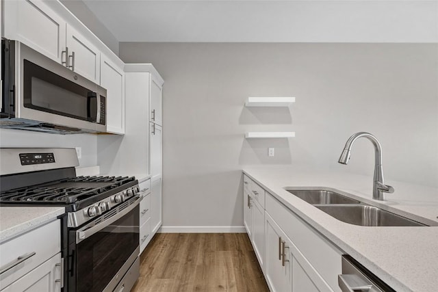 kitchen with stainless steel appliances, light wood-style flooring, white cabinets, a sink, and light stone countertops