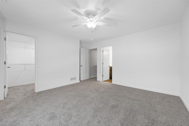 unfurnished bedroom featuring ceiling fan, light colored carpet, visible vents, baseboards, and a walk in closet