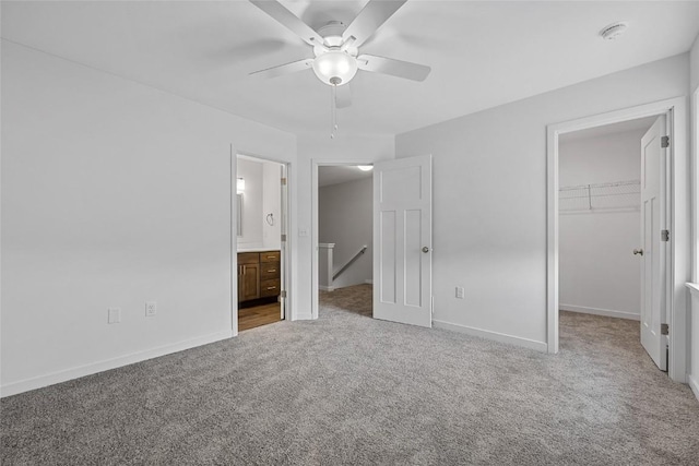 unfurnished bedroom with baseboards, connected bathroom, a walk in closet, carpet floors, and a closet