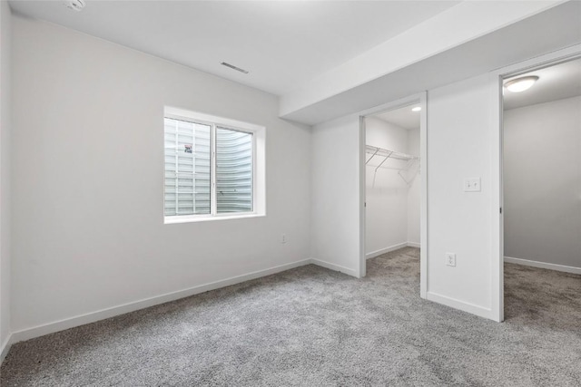 unfurnished bedroom with a walk in closet, visible vents, light carpet, and baseboards