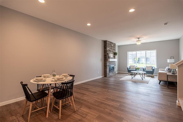 dining space featuring dark wood-style flooring, a fireplace, a ceiling fan, and baseboards