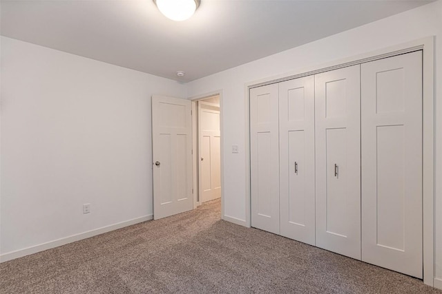 unfurnished bedroom with a closet, light carpet, and baseboards