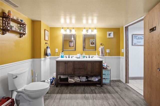 230 E Market St, Lisbon, IA 52253 - bathroom with toilet, a wainscoted wall, wood finished floors, a sink, and visible vents