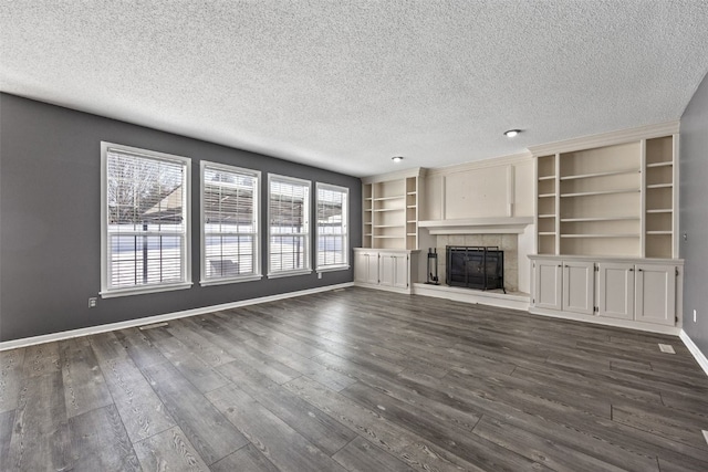 unfurnished living room with dark wood-style floors, a textured ceiling, a tiled fireplace, and baseboards