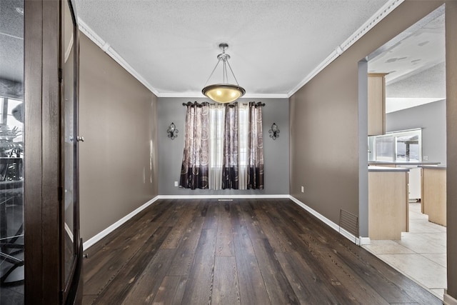 unfurnished dining area with baseboards, a textured ceiling, ornamental molding, and wood finished floors