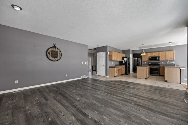 kitchen with dark countertops, a kitchen island, open floor plan, decorative light fixtures, and stainless steel appliances