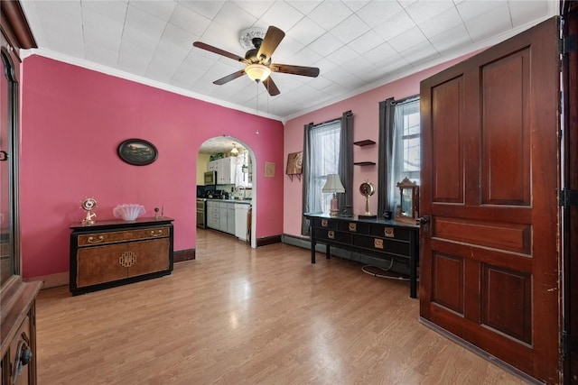 interior space featuring light wood-style flooring, arched walkways, baseboards, and ornamental molding