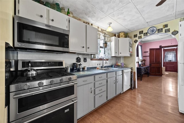 kitchen with arched walkways, appliances with stainless steel finishes, white cabinetry, a sink, and light wood-type flooring