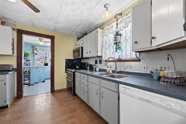 kitchen featuring white cabinets, dark countertops, stainless steel appliances, light wood-style floors, and a sink