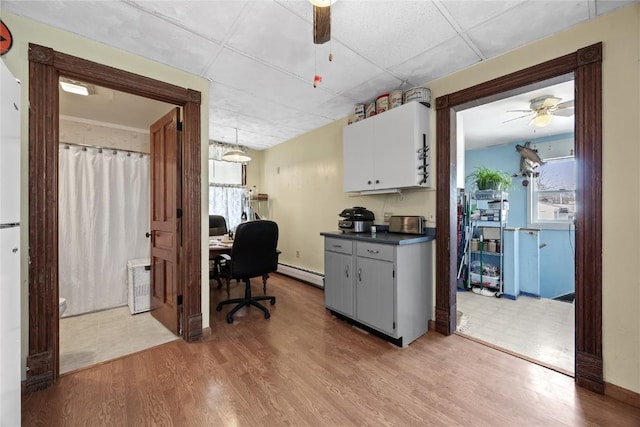 office space featuring light wood-type flooring, ceiling fan, a baseboard heating unit, and a paneled ceiling