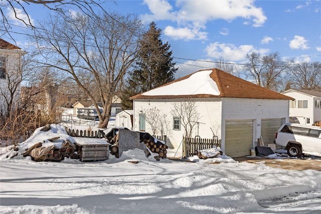 view of snowy exterior with a garage and fence