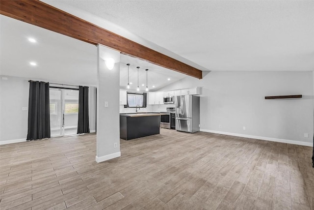 kitchen featuring white cabinets, appliances with stainless steel finishes, open floor plan, decorative light fixtures, and light countertops