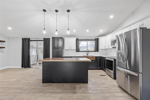 kitchen featuring white cabinets, lofted ceiling, appliances with stainless steel finishes, decorative light fixtures, and a center island