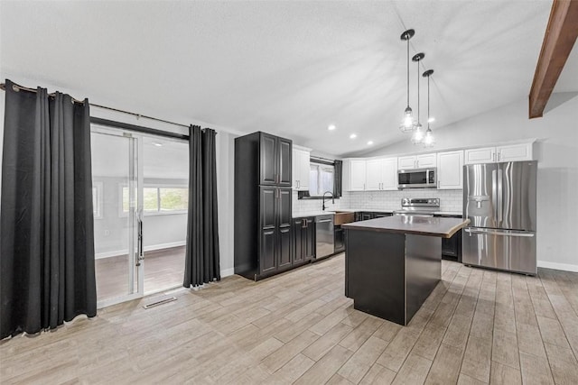 kitchen featuring a center island, stainless steel appliances, tasteful backsplash, hanging light fixtures, and lofted ceiling with beams