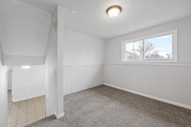 empty room featuring wainscoting, light colored carpet, a textured ceiling, and light tile patterned floors