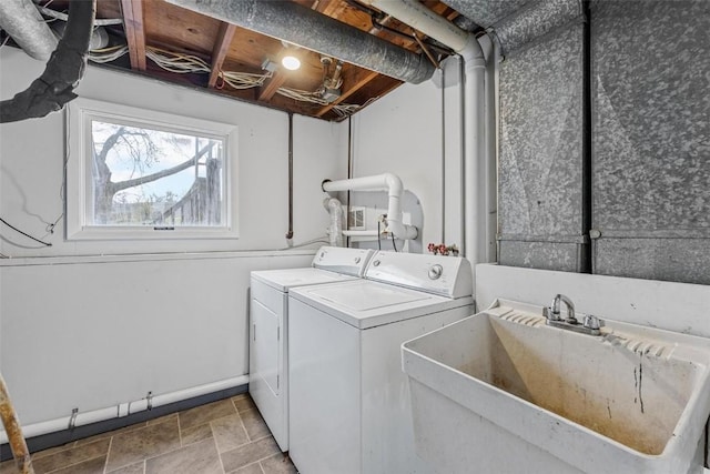 clothes washing area featuring laundry area, baseboards, washer and clothes dryer, stone finish floor, and a sink