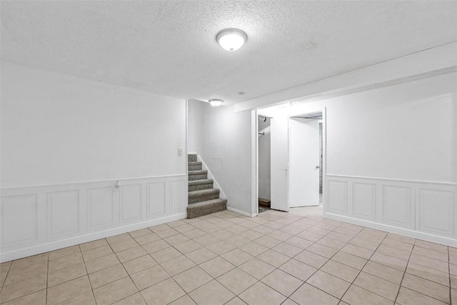 finished below grade area featuring a textured ceiling, stairway, and a wainscoted wall