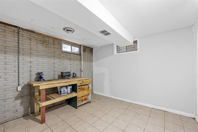 below grade area featuring brick wall, visible vents, and baseboards