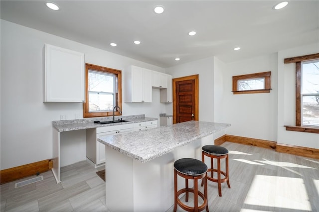 kitchen featuring visible vents, a kitchen island, light stone countertops, white cabinetry, and a sink