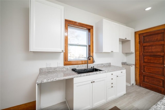 kitchen featuring recessed lighting, white cabinets, a sink, light stone countertops, and baseboards