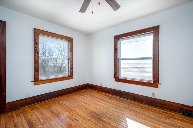 empty room with a ceiling fan, visible vents, baseboards, and wood finished floors