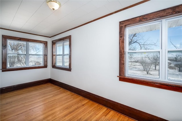 spare room featuring baseboards, crown molding, and light wood finished floors