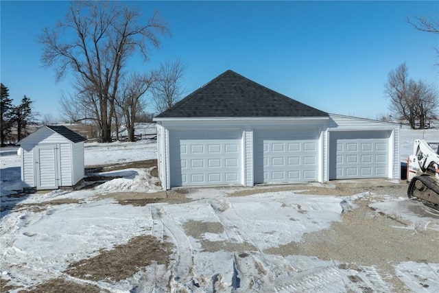 snow covered garage featuring a storage unit and a detached garage