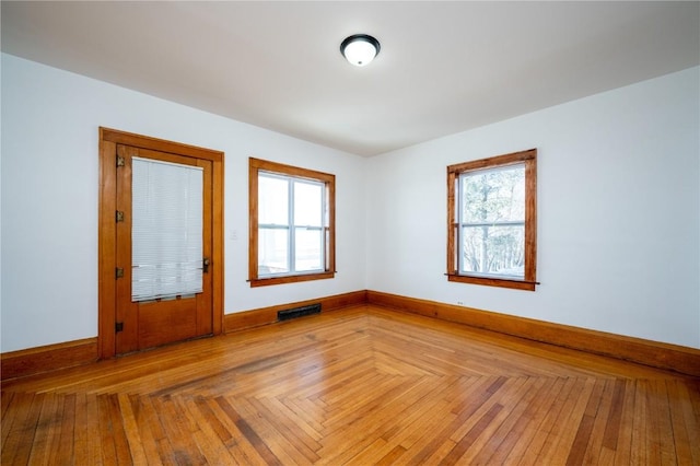 empty room featuring parquet floors, baseboards, visible vents, and a wealth of natural light