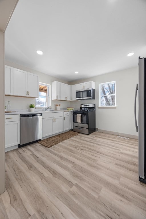 kitchen with appliances with stainless steel finishes, light countertops, light wood-type flooring, white cabinetry, and recessed lighting